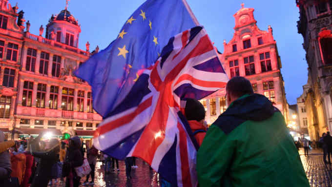 Pedestrians wave European Union (EU) and British Union flags in Grand Place square in Brussels, Belgium, on Thursday, Jan. 30, 2020. The European Parliament approved Prime Minister Boris Johnson’s Brexit deal, clearing the way for the U.K. to leave the EU on Jan. 31 with an agreement that, for the time being, will avoid a chaotic rupture. Photographer: Geert Vanden Wijngaert/Bloomberg