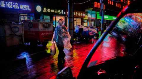A woman wearing a raincoat walks down a street in Beijing