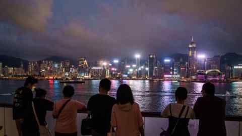 People with their backs to the camera look at Hong Kong’s Victoria Harbour at night. Lit up skyscrapers can be seen in the distance