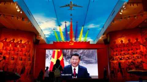 Los visitantes se paran frente a una pantalla gigante que muestra un retrato de Xi Jinping, en el Museo Militar de la Revolución Popular China en Beijing.  En el techo se proyecta la imagen de un avión con estelas de humo multicolor.