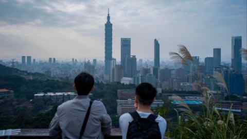 Two people, seen from behind, look out at a skyline with tall skyscrapers