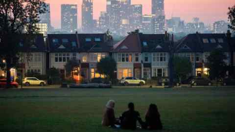 Three people in fading light with a viewpoint of terraced houses and in the distance, the growing development at Nine Elms at Battersea, seen from Ruskin Park in Lambeth