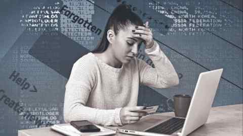 Young woman in front of a laptop.  She is upset and looks at a credit card and touches her forehead