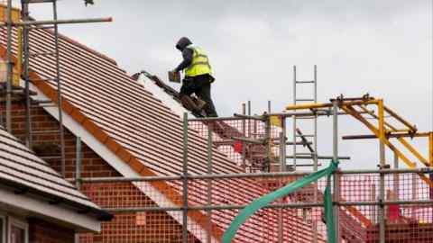 A construction worker fixes tiles to the roof of a new house