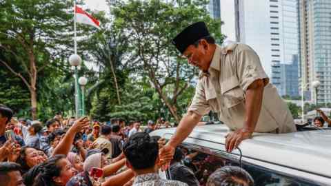 Prabow Subianto leans out of the sun roof of a car to shake hands with a member of a crowd of supporters