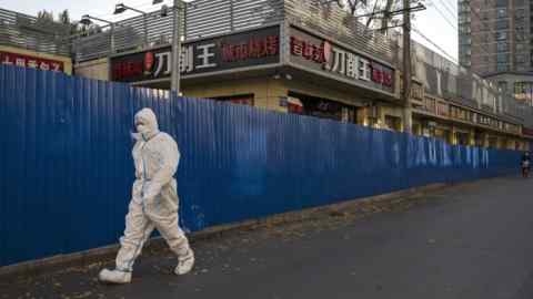 An epidemic control worker wearing protective equipment walks along a street in a locked-down area of Beijing,