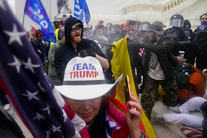 A woman wears a hat with the words Team Trump, as rioters try to break through a police barrier 